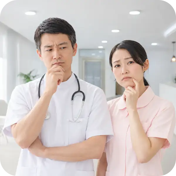 診察室で腕を組み、あごに手を当てて困った表情を浮かべる医師と看護師（地図とサイトの情報のずれに気づかず、患者様の候補から外れてしまうことを表すイメージ）